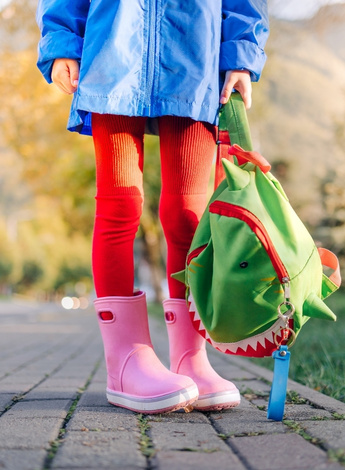 The image is of a child's legs. The child has knocked knees. A backpack held by the child is dangling down. 